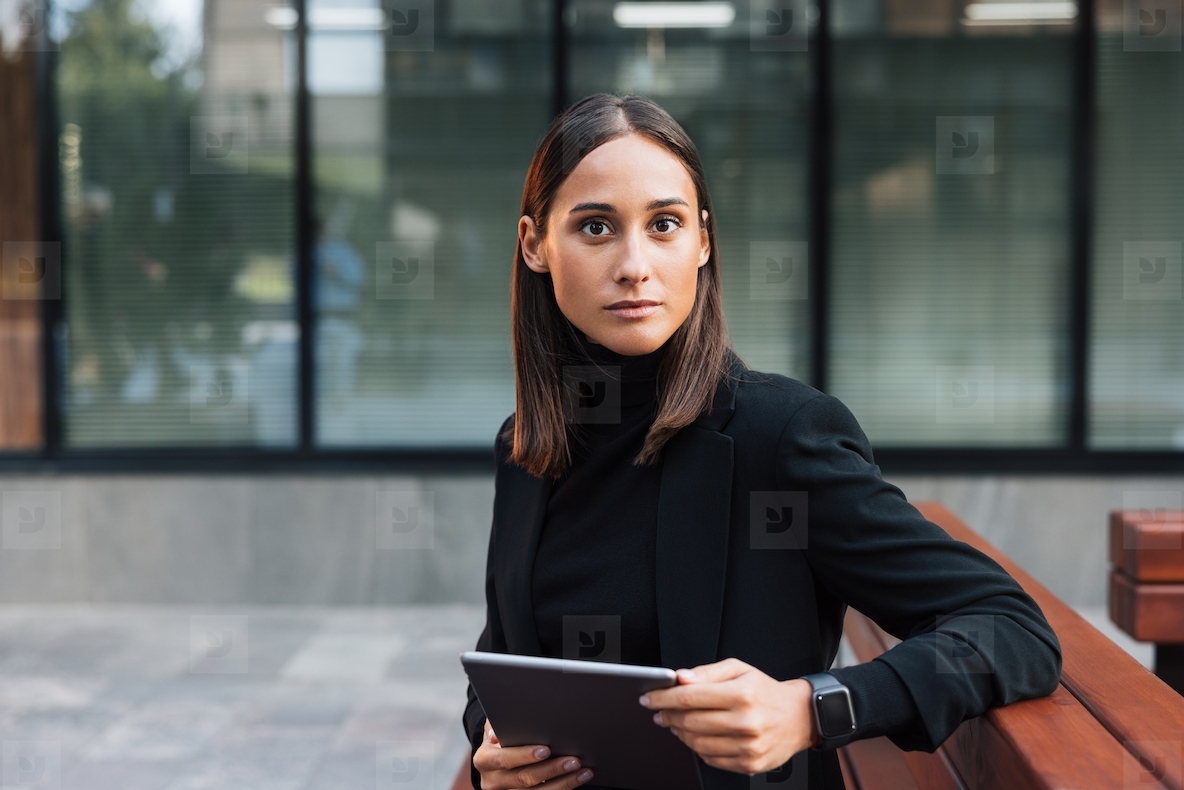 Portrait of a young brunette businesswoman wearing stylish black formal clothes Female entertainer looking at camera while sitting outside