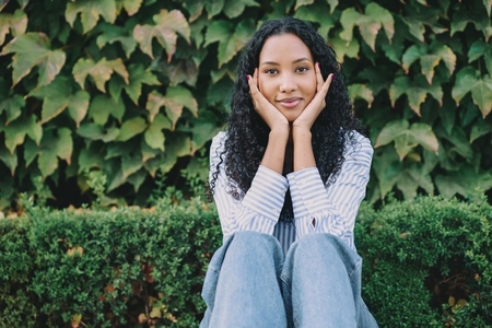 A Smiling Woman Posing Outdoors Against a Backdrop of Lush Greenery in Natures Beauty
