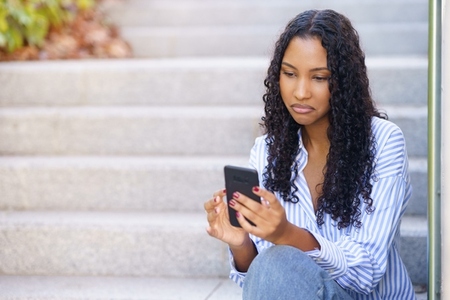 A young woman is actively using her smartphone while sitting comfortably on the steps outdoors