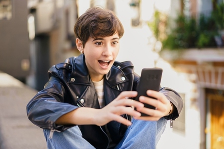 A cheerful young person is happily engaging with their smartphone in a bustling urban environment A cheerful young person is happily engaging with their smartphone in a bustling urban environment