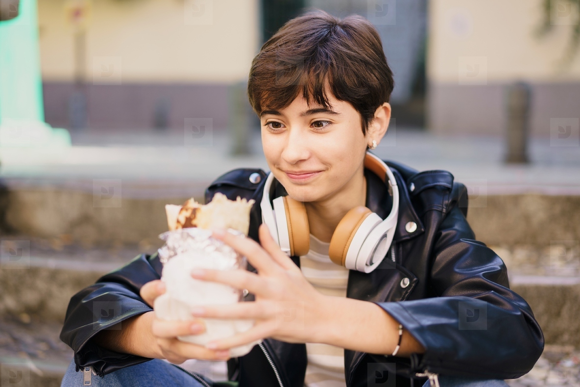 A Young Woman Fully Enjoying a Delicious Dessert While Wearing Headphones in an Urban Setting