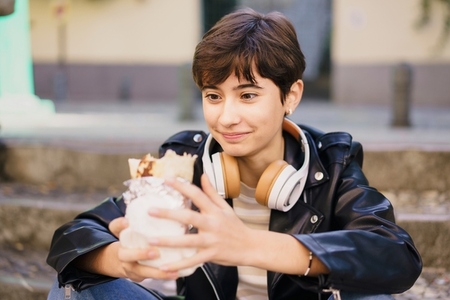 A Young Woman Fully Enjoying a Delicious Dessert While Wearing Headphones in an Urban Setting