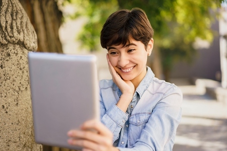 A Young Woman Happily Enjoying a Video Call Outdoors Using Her Tablet in the Sunshine