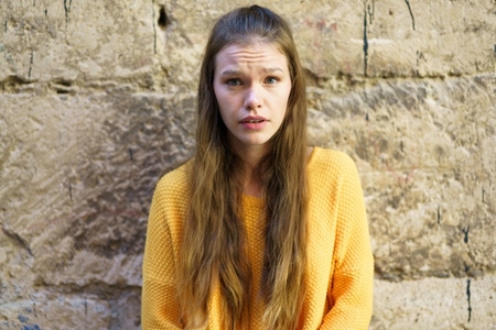 A portrait of a young woman in a yellow sweater posed elegantly against a textured wall A portrait of a young woman in a yellow sweater posed elegantly against a textured wall