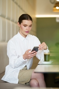 Concentrated businesswoman using phone sitting in a modern cafeteria