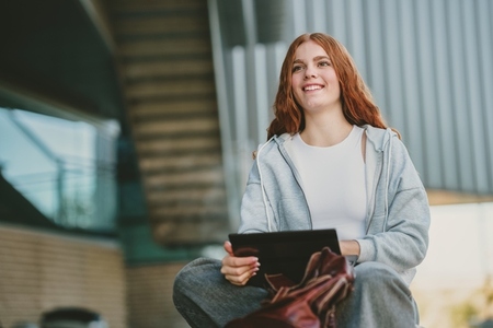 A Young Woman Delightfully Engaging with Her Tablet in a Vibrant Urban Outdoor Environment A Young Woman Delightfully Engaging with Her Tablet in a Vibrant Urban Outdoor Environment