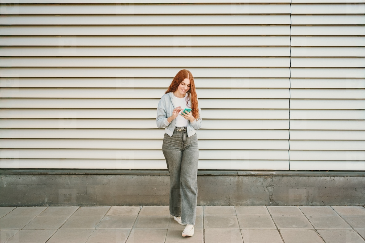 A young woman is calmly walking in an urban setting while using her phone for connection