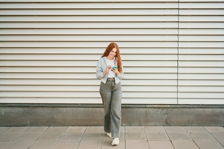 A young woman is calmly walking in an urban setting while using her phone for connection A young woman is calmly walking in an urban setting while using her phone for connection