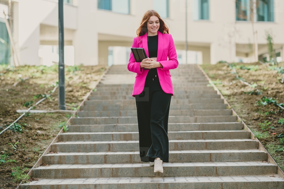 A Confident Businesswoman is Walking Downstairs while Wearing a Bright Pink Blazer