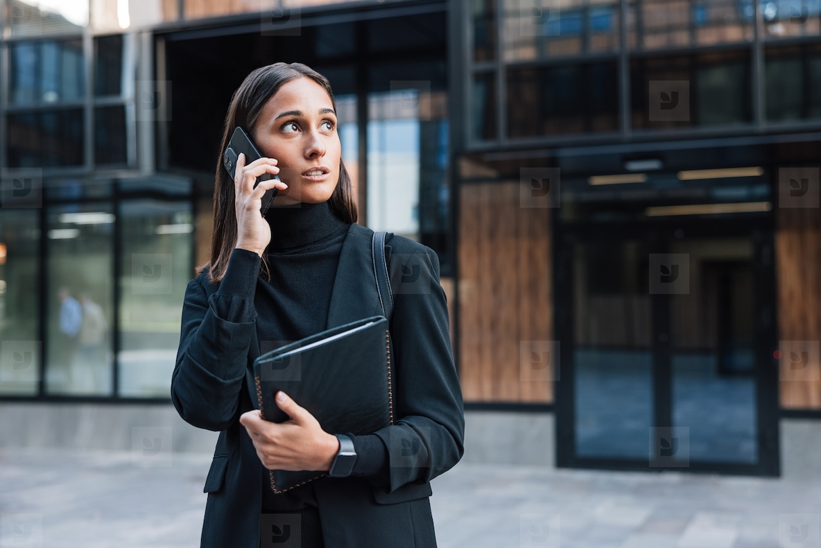 Confident female entrepreneur talking on mobile phone wearing stylish black formal clothes