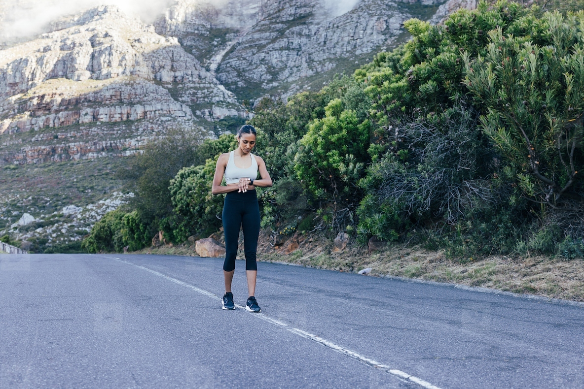 Full length of young slim female standing on abandoned road against mountain and checking smart watches