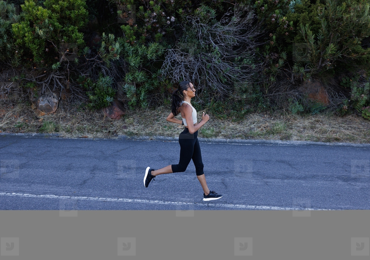 High angle of young slim female running on abandoned road  Slim female jogging solo on road