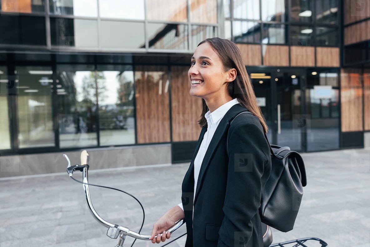 Happy female with bicycle and backpack walking outside  Young smiling businesswoman with a bicycle walking on the street