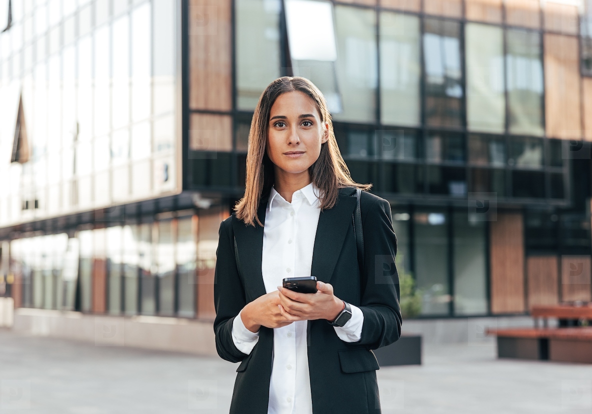 Portrait of a young woman in formal wear standing outside against an office building