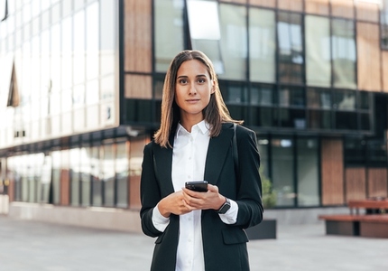 Portrait of a young woman in formal wear standing outside against an office building