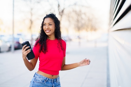 A Cheerful Young Woman is Happily Enjoying a Beautiful Day Out While Using Her Smartphone