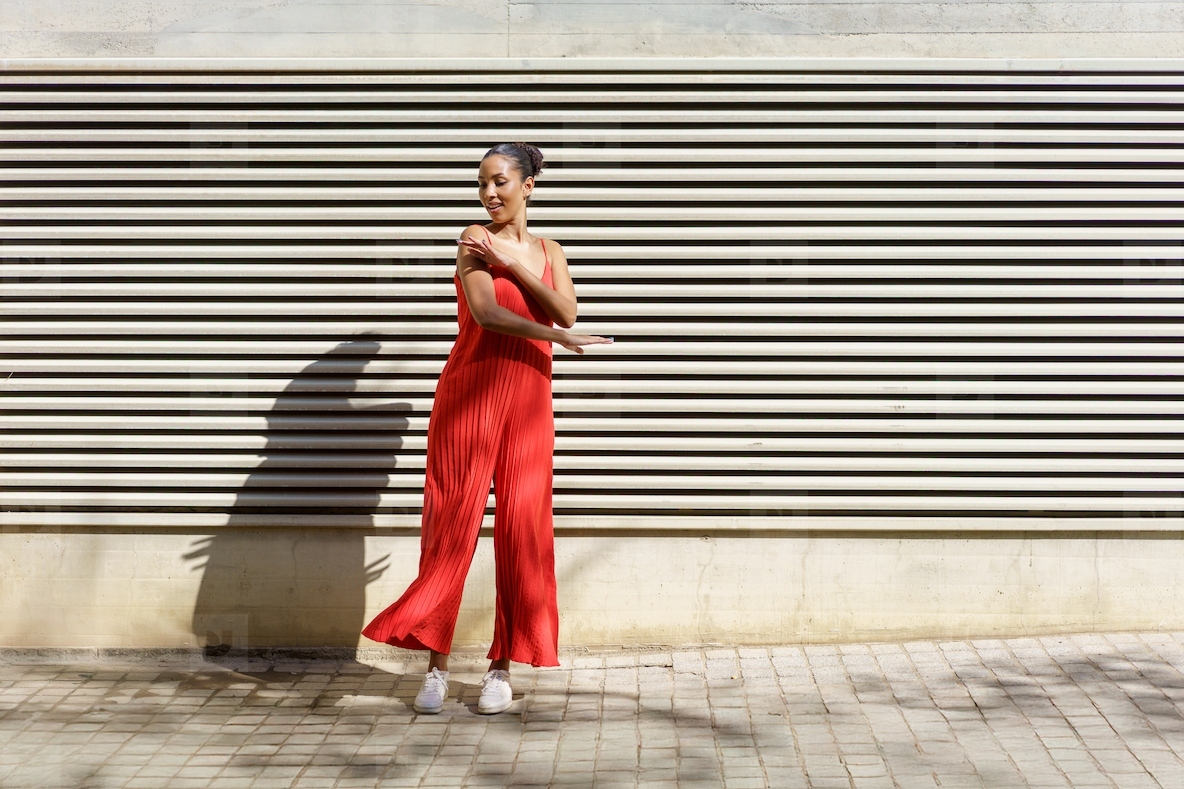 A Young Woman Dressed in a Stylish Red Jumpsuit is Dancing Happily Against a Textured Wall