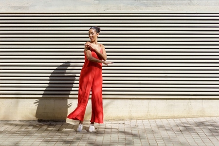 A Young Woman Dressed in a Stylish Red Jumpsuit is Dancing Happily Against a Textured Wall