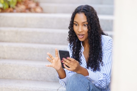 A young woman is happily engaged with her smartphone while sitting on outdoor steps A young woman is happily engaged with her smartphone while sitting on outdoor steps