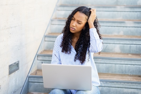 A young woman who appears frustrated is working diligently on her laptop in a modern setting
