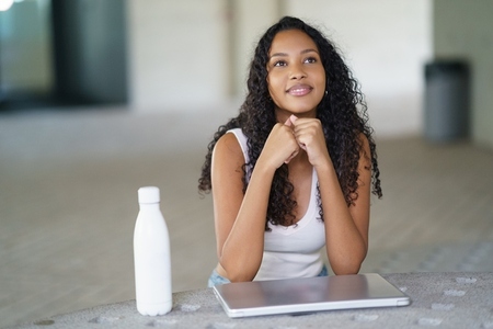 A thoughtful young woman with a laptop and a water bottle sits in a modern  stylish space