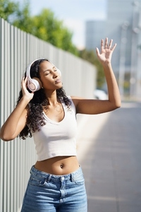 A joyful and happy young woman is enjoying music outdoors while wearing stylish headphones A joyful and happy young woman is enjoying music outdoors while wearing stylish headphones