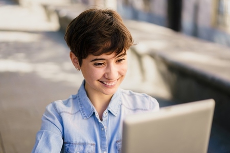 A Young Woman Happily Utilizing Her Laptop Outdoors While Enjoying the Beautiful Day A Young Woman Happily Utilizing Her Laptop Outdoors While Enjoying the Beautiful Day
