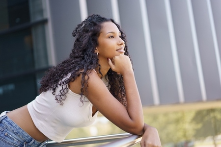 A thoughtful young woman with curly hair finds contemplation in an urban outdoor setting