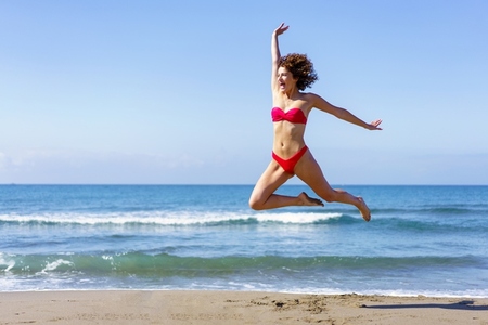 Carefree woman in swimwear jumping on beach