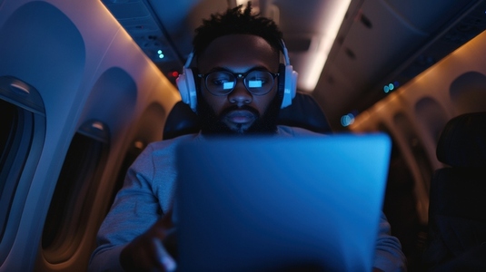 person wearing headphones works on laptop during night flight