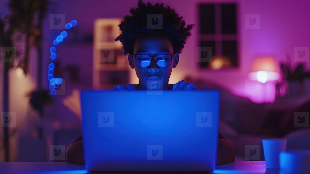 Teenager focused on laptop in dimly lit room with blue light