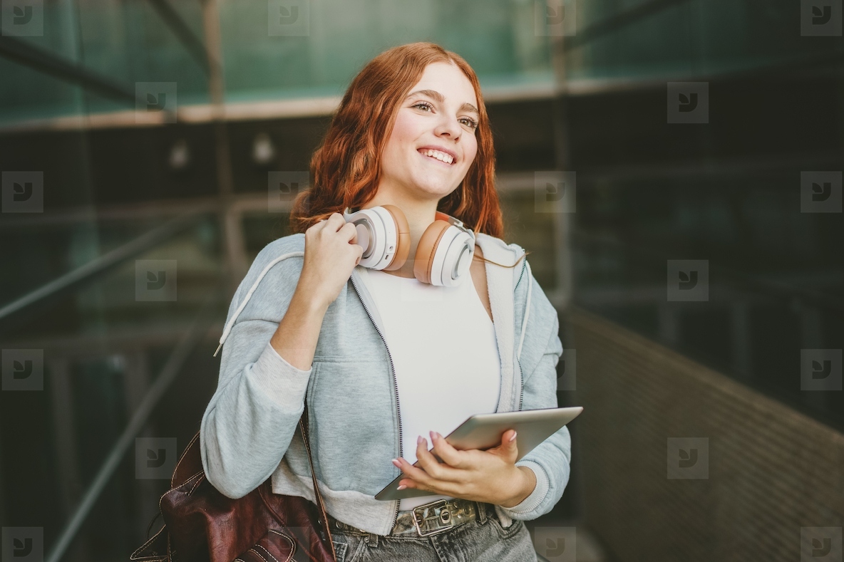 A Smiling Young Woman Wearing Headphones and Using a Tablet in a Vibrant Urban Setting
