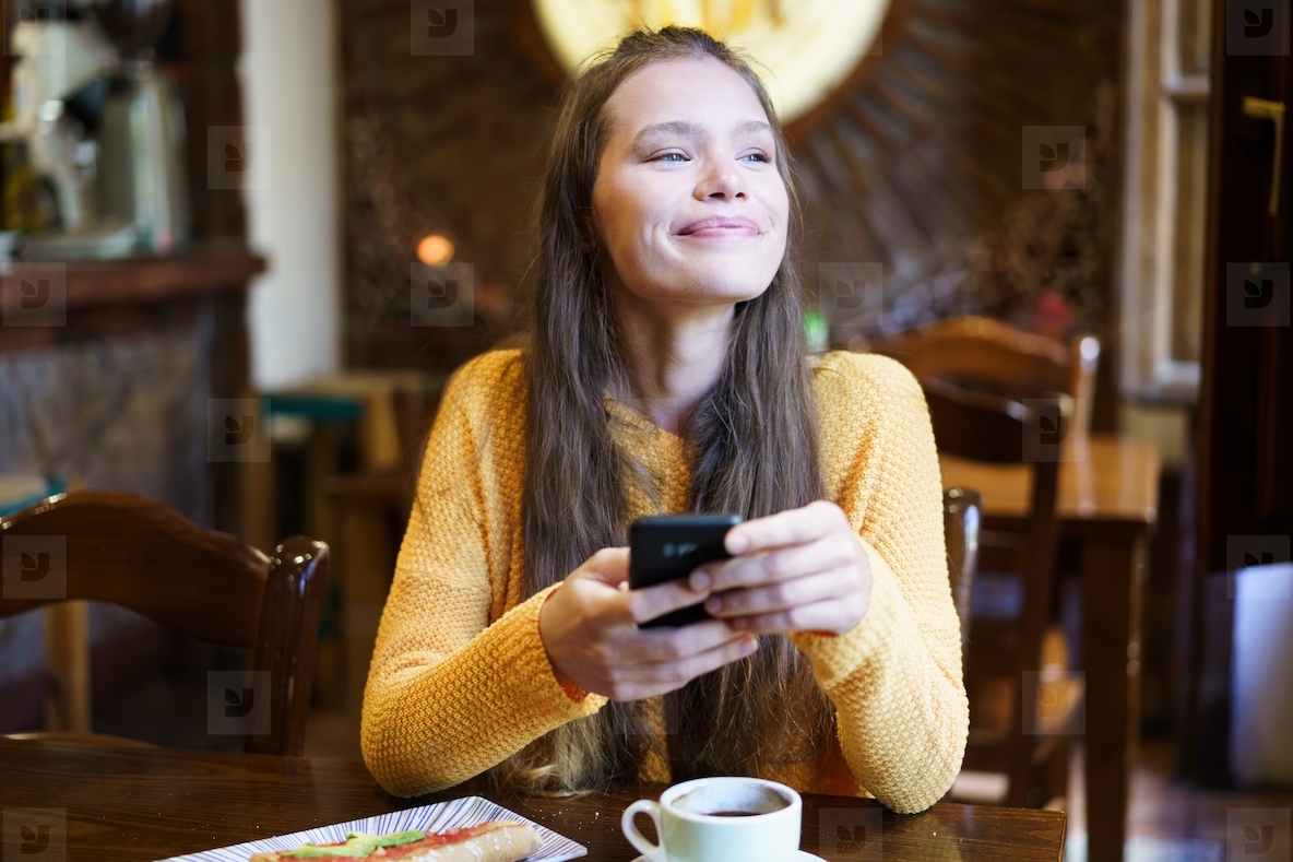 Young Woman Enjoying Coffee and Texting in Cozy Caf