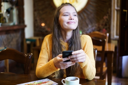 Young Woman Enjoying Coffee and Texting in Cozy Caf