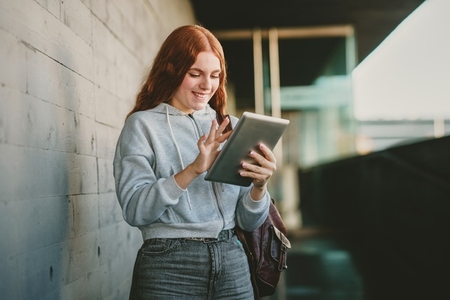A young woman is happily engaged with her tablet while in a vibrant urban setting
