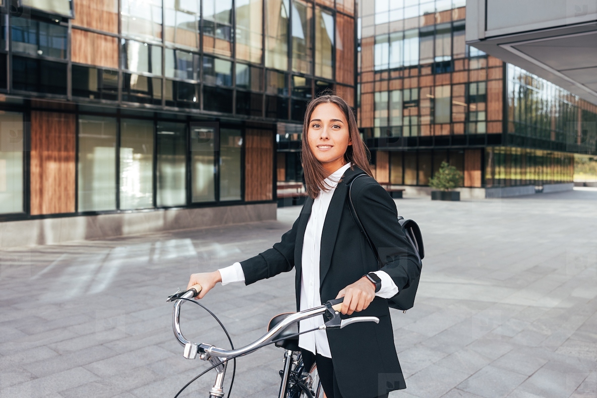 Portrait of a young woman in formal wear looking at camera and holding bicycle handlebars  Businesswoman during her ride to the office