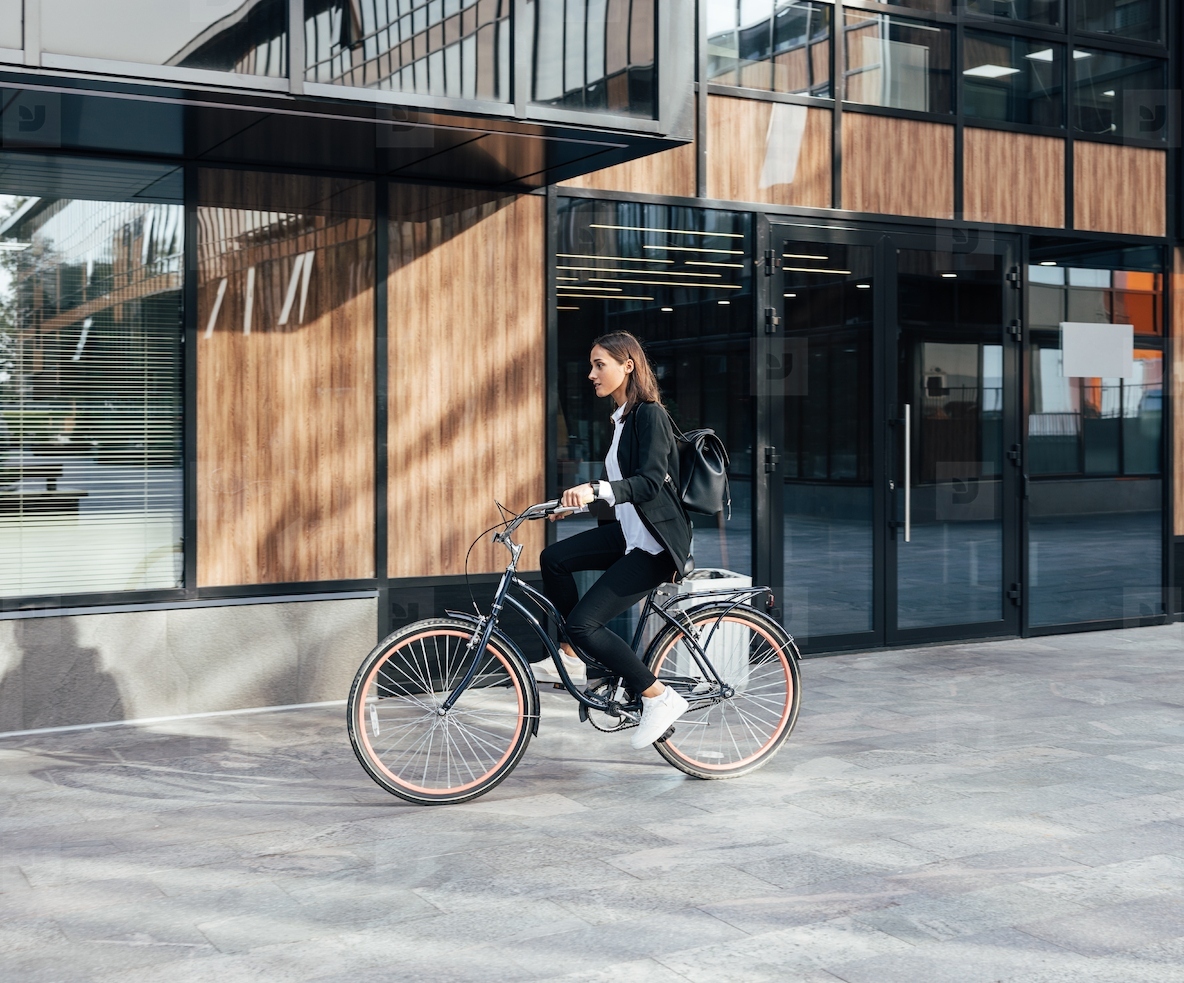 Woman in formal wear riding a bicycle against a business building  Businesswoman is going to work on a bicycle