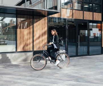 Woman in formal wear riding a bicycle against a business building  Businesswoman is going to work on a bicycle