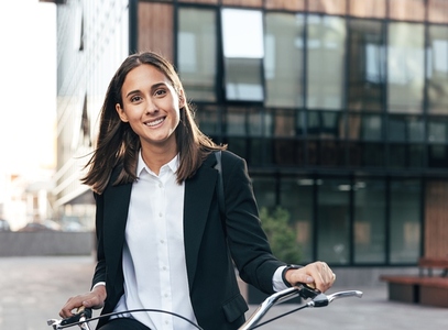 Portrait of young female with a bicycle and formal wear standing in the city and looking at camera