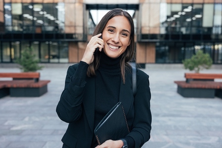 Portrait of a smiling woman employee in black formal wear  Happy businesswoman wearing stylish formal wear  talking on mobile phone and looking at camera