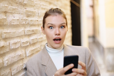A Surprised Woman Holding Her Phone while in an Urban Setting Full of Life and Vibrance