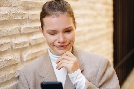 A young woman is engaged and absorbed with her smartphone while situated in a cozy urban setting A young woman is engaged and absorbed with her smartphone while situated in a cozy urban setting