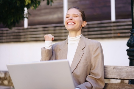 A Joyful Businesswoman is Happily Celebrating Her Success Outdoors Near a Bench in Nature