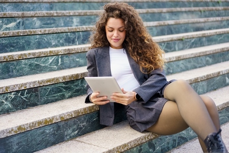 A Young Professional Woman Sitting on the Steps While Using a Tablet Device to Work