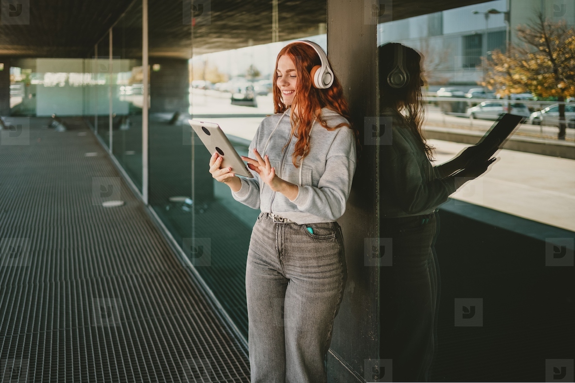 A Young Woman in a City Environment Enjoying Music While Wearing Headphones and Using a Tablet