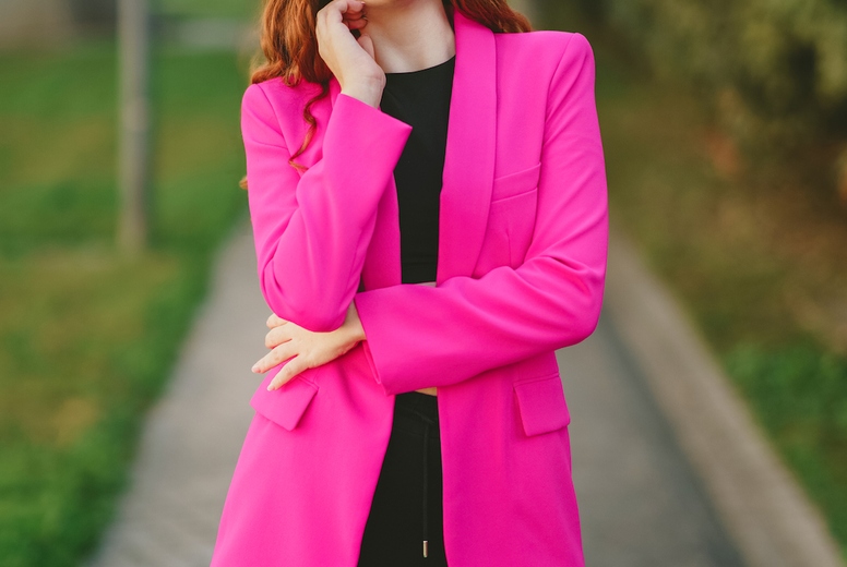 A Stylish Young Woman Wearing a Bright Pink Blazer Stands on a Vibrant Urban Pathway
