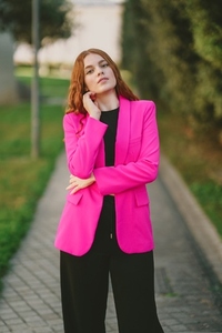 A Stylish Young Woman Wearing a Bright Pink Blazer Stands on a Vibrant Urban Pathway A Stylish Young Woman Wearing a Bright Pink Blazer Stands on a Vibrant Urban Pathway