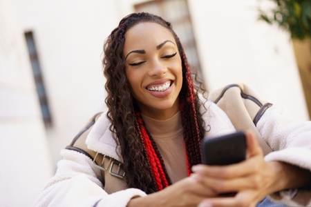 A Young Woman is Enjoying Her Time on Her Smartphone While Relaxing Outdoors Under the Sun