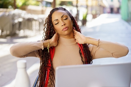 A Stressed Woman Engaging in Stretching Exercises at an Outdoor Cafe While Using a Laptop