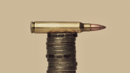UK Defense Spending still life of bullet cartridge on stack of British Pound coins
